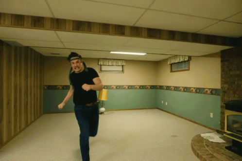 A Man In A Black Shirt Is Running In A Room GIF