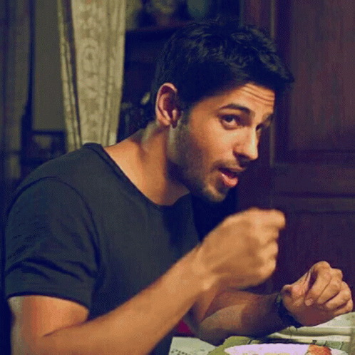 A Man In A Black Shirt Is Sitting At A Table And Eating Food GIF