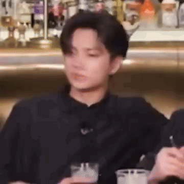 A Man In A Black Shirt Is Sitting At A Table With A Drink In His Hand . GIF