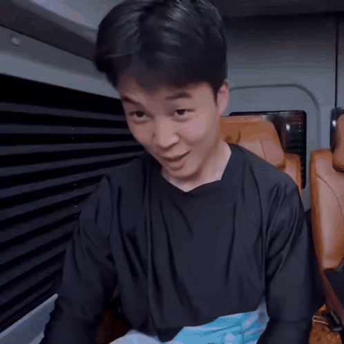 A Man In A Black Shirt Is Sitting In A Car With A Foreign Language Behind Him GIF