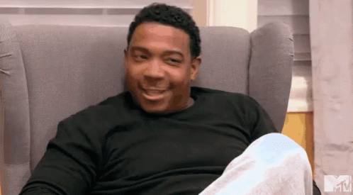 A Man In A Black Shirt Is Sitting In A Chair With A Mtv Logo In The Background GIF