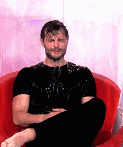 A Man In A Black Shirt Is Sitting In A Red Chair With Water Dripping Off His Face GIF