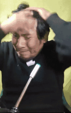 A Man In A Black Shirt Is Sitting In Front Of A Microphone And Scratching His Head GIF