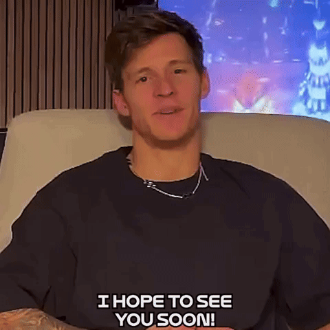 A Man In A Black Shirt Is Sitting On A Couch And Saying " I Hope To See You Soon " GIF