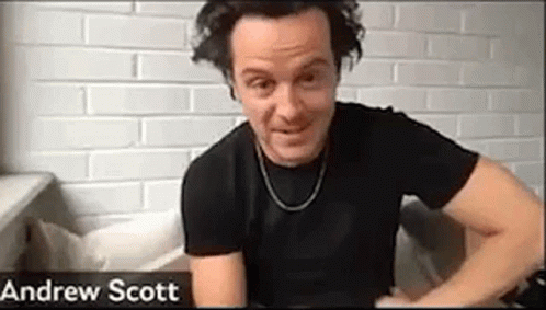 A Man In A Black Shirt Is Sitting On A Couch In Front Of A Brick Wall . GIF