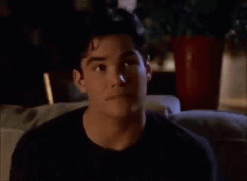 A Man In A Black Shirt Is Sitting On A Couch Looking At Something GIF