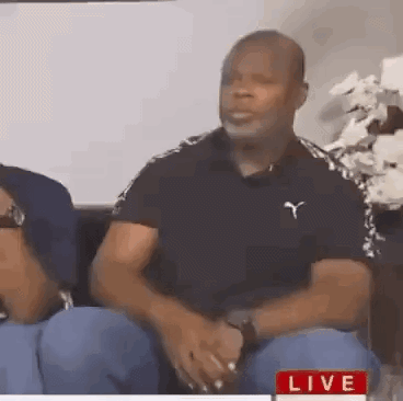 A Man In A Black Shirt Is Sitting On A Couch With A Woman . GIF