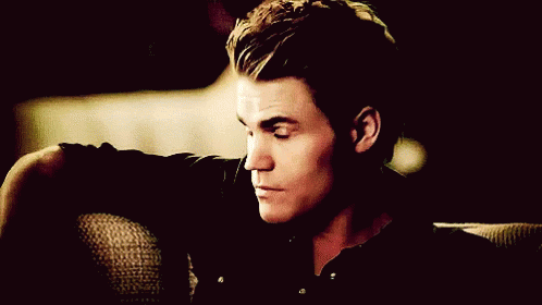 A Man In A Black Shirt Is Sitting On A Couch With His Head Resting On His Arm GIF