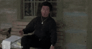 A Man In A Black Shirt Is Sitting On A Wooden Bench GIF