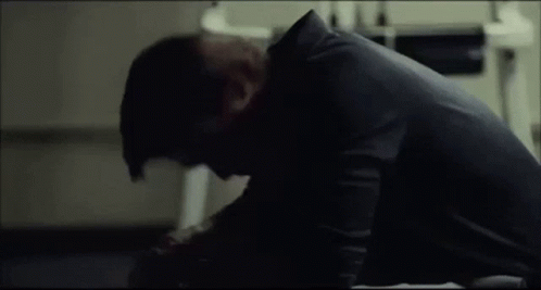 A Man In A Black Shirt Is Sitting On The Floor With His Head On His Knees . GIF