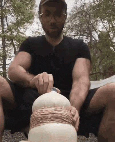 A Man In A Black Shirt Is Sitting On The Ground Holding A Bottle GIF