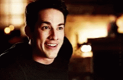 a man in a black shirt is smiling in a dark room .