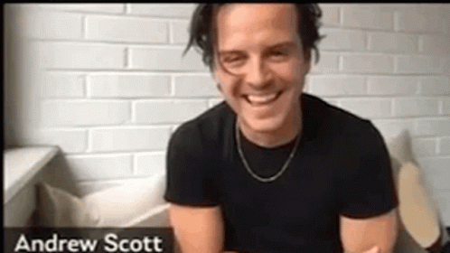 A Man In A Black Shirt Is Smiling In Front Of A Brick Wall . GIF