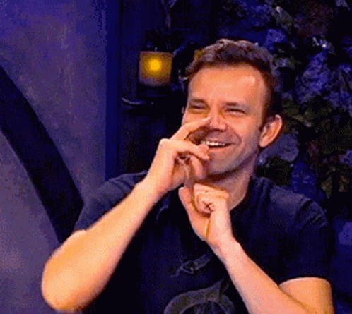 A Man In A Black Shirt Is Smiling While Holding His Hand To His Nose . GIF