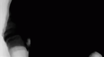 A Man In A Black Shirt Is Standing In A Black And White Photo . GIF