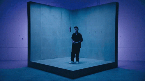 A Man In A Black Shirt Is Standing In A Blue Room GIF