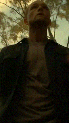 A Man In A Black Shirt Is Standing In A Dark Forest GIF