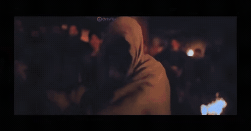 A Man In A Black Shirt Is Standing In A Dark Room With A Blurred Background . GIF