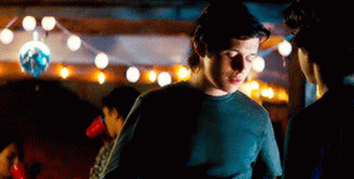 A Man In A Black Shirt Is Standing In A Dark Room With A Disco Ball In The Background . GIF