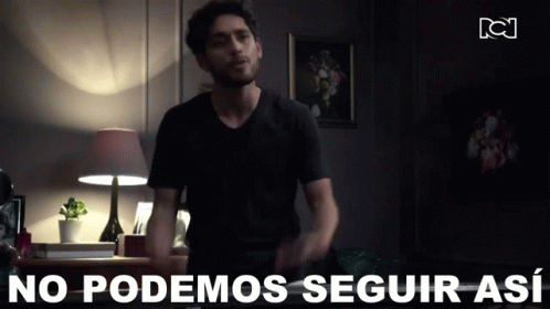 A Man In A Black Shirt Is Standing In A Dark Room With The Words " No Podemos Seguir Así " Behind Him GIF
