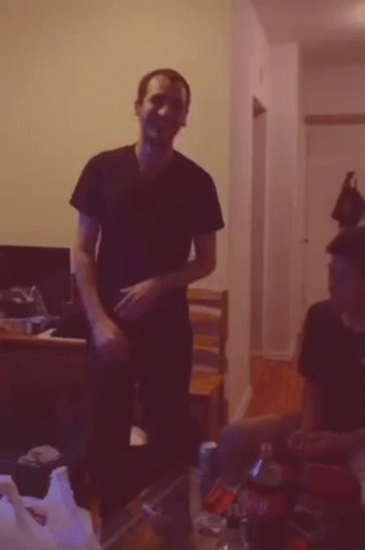 A Man In A Black Shirt Is Standing In A Dark Room GIF