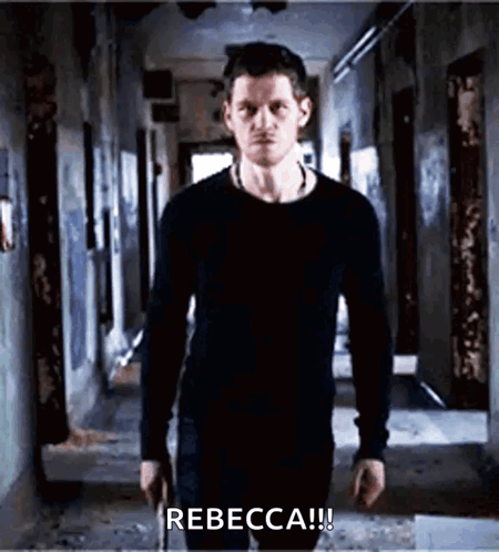 A Man In A Black Shirt Is Standing In A Hallway Holding A Gun And Says Rebecca ! GIF