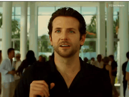 A Man In A Black Shirt Is Standing In A Hallway With A Vibezmaxx Watermark On The Bottom Right GIF
