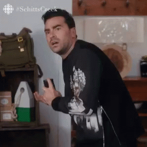 A Man In A Black Shirt Is Standing In A Kitchen Holding A Cell Phone In His Hand . GIF