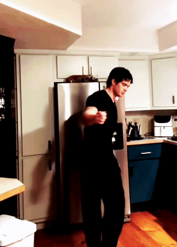 a man in a black shirt is standing in a kitchen near a stainless steel refrigerator