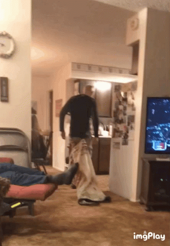 A Man In A Black Shirt Is Standing In A Living Room Next To A Tv And A Clock GIF