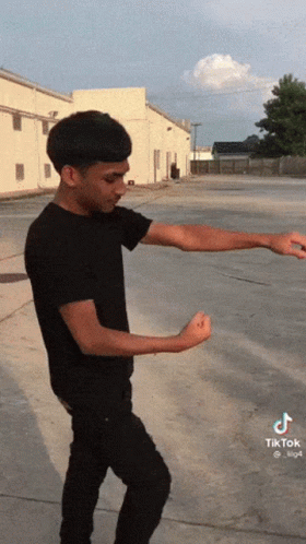 a man in a black shirt is standing in a parking lot with his arms outstretched and a tiktok logo on the bottom left