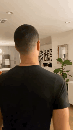 A Man In A Black Shirt Is Standing In A Room GIF