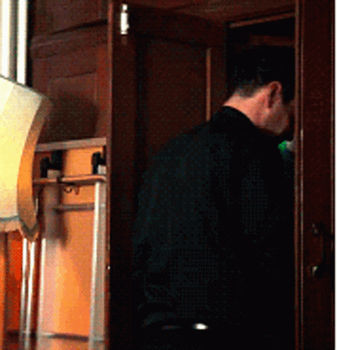 A Man In A Black Shirt Is Standing In A Room GIF