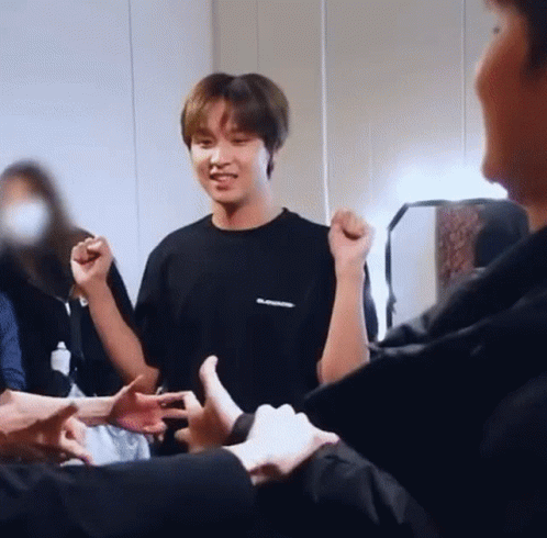 A Man In A Black Shirt Is Standing In A Room Surrounded By People And Giving A Thumbs Up . GIF