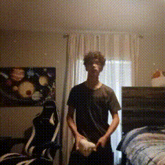A Man In A Black Shirt Is Standing In A Room With A Painting On The Wall . GIF