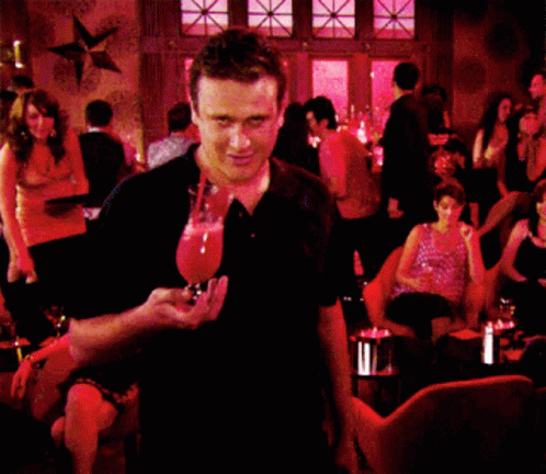 A Man In A Black Shirt Is Standing In Front Of A Crowd Of People GIF