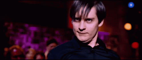 A Man In A Black Shirt Is Standing In Front Of A Crowd Of People GIF
