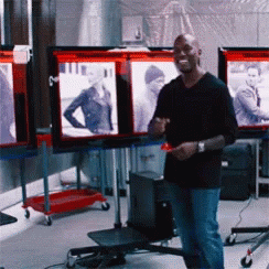 A Man In A Black Shirt Is Standing In Front Of A Display Of Pictures GIF