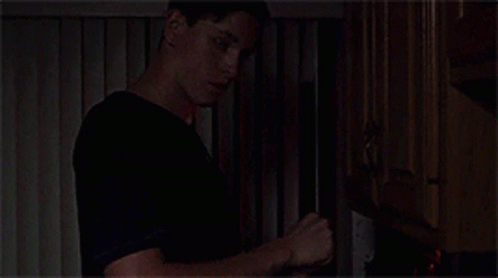 A Man In A Black Shirt Is Standing In Front Of A Fireplace . GIF