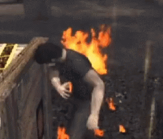 A Man In A Black Shirt Is Standing In Front Of A Large Fire . GIF