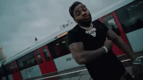 A Man In A Black Shirt Is Standing In Front Of A Red Train . GIF