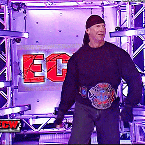 A Man In A Black Shirt Is Standing In Front Of A Sign That Says Ecw GIF