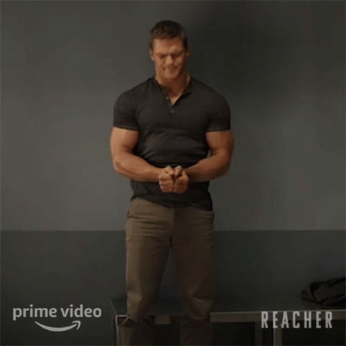 A Man In A Black Shirt Is Standing In Front Of A Sign That Says Prime Video Reacher GIF