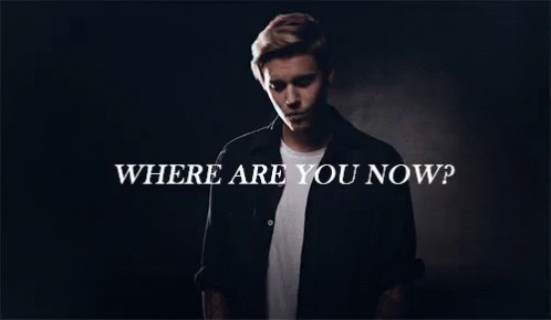 A Man In A Black Shirt Is Standing In Front Of A Sign That Says Where Are You Now GIF