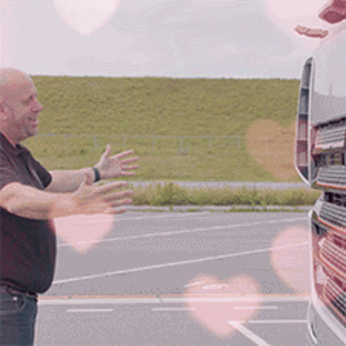 A Man In A Black Shirt Is Standing In Front Of A Truck With His Arms Outstretched GIF
