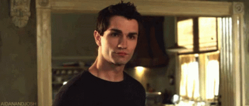 A Man In A Black Shirt Is Standing In Front Of A Window With A Caption That Says Aidanandjosh GIF