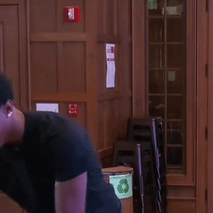 A Man In A Black Shirt Is Standing In Front Of A Wooden Door And Smiling . GIF