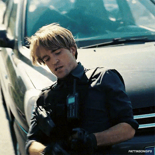 A Man In A Black Shirt Is Standing Next To A Black Car Holding A Walkie Talkie GIF