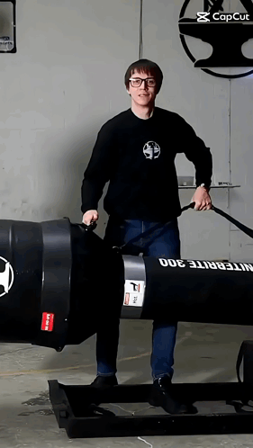 A Man In A Black Shirt Is Standing Next To A Large Black Barrel That Says Integrite 300 On It GIF