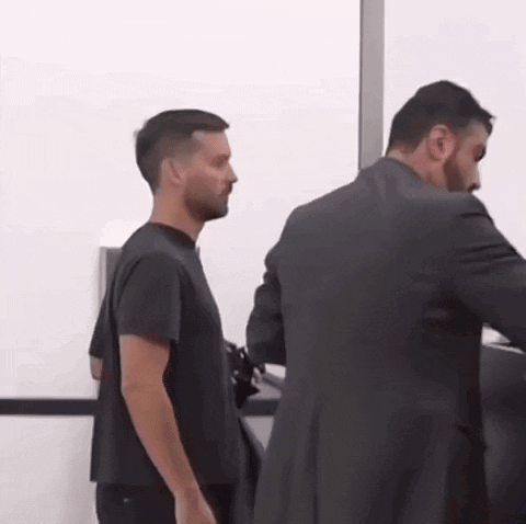 A Man In A Black Shirt Is Standing Next To A Man In A Suit GIF